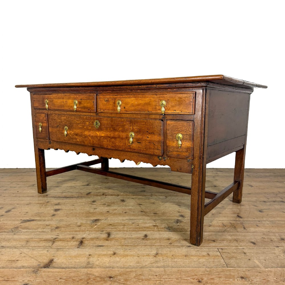 An antique oak serving table featuring brass drop handles, multiple drawer compartments, a scalloped apron, and straight legs connected by stretchers. View II