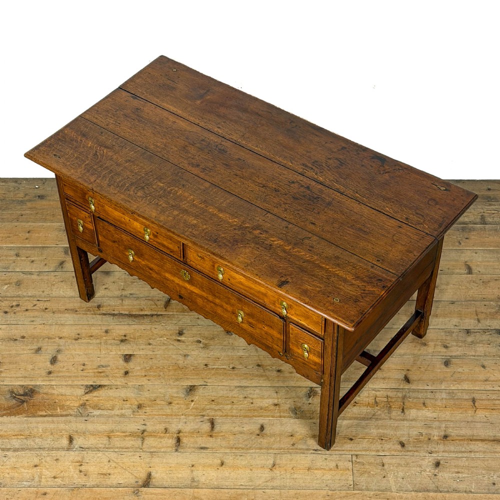 An antique oak serving table featuring brass drop handles, multiple drawer compartments, a scalloped apron, and straight legs connected by stretchers. View III