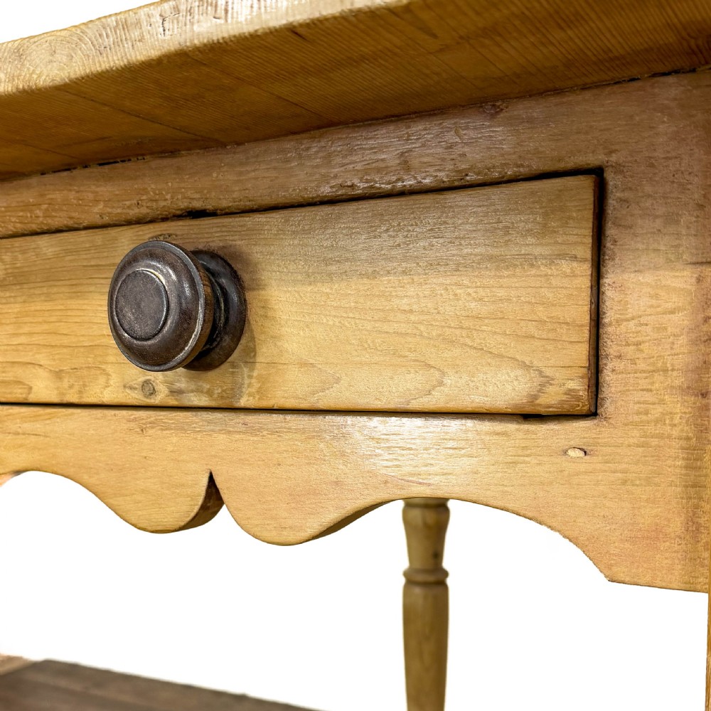 An antique honey pine kitchen table featuring hand-turned legs, a scalloped apron, and a single end drawer with a dark turned wooden knob. View V