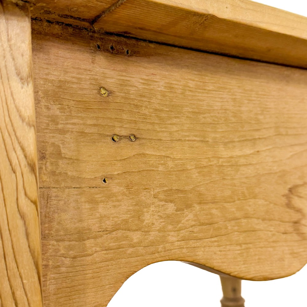 An antique honey pine kitchen table featuring hand-turned legs, a scalloped apron, and a single end drawer with a dark turned wooden knob. View VI