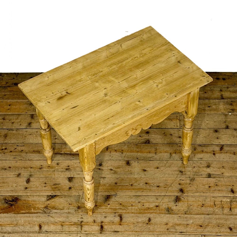 An antique honey pine kitchen table featuring hand-turned legs, a scalloped apron, and a single end drawer with a dark turned wooden knob. View VII