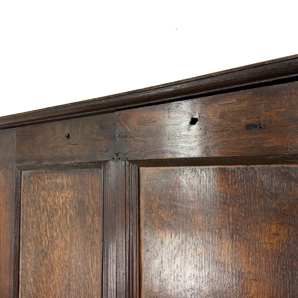 A two-tier dark oak cupboard featuring relief carvings, lion masks, geometric panelled doors, and a decorative carved pediment. View V
