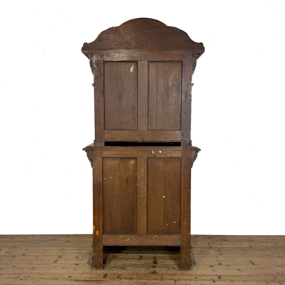 A two-tier dark oak cupboard featuring relief carvings, lion masks, geometric panelled doors, and a decorative carved pediment. View X