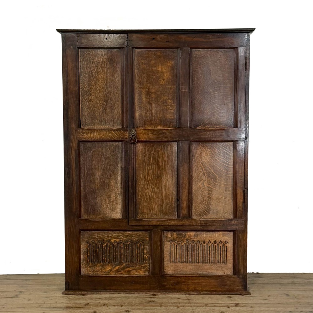 A two-tier dark oak cupboard featuring relief carvings, lion masks, geometric panelled doors, and a decorative carved pediment. View XIII