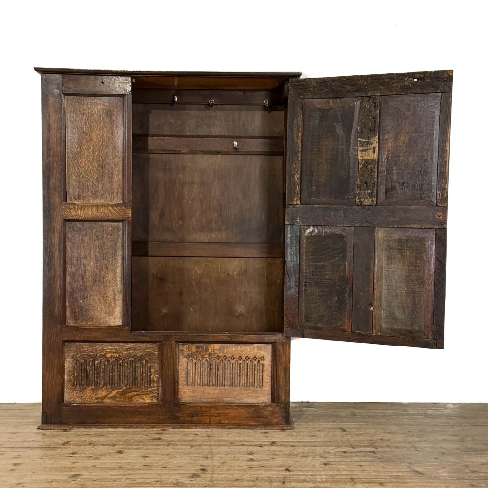 A two-tier dark oak cupboard featuring relief carvings, lion masks, geometric panelled doors, and a decorative carved pediment. View XIV