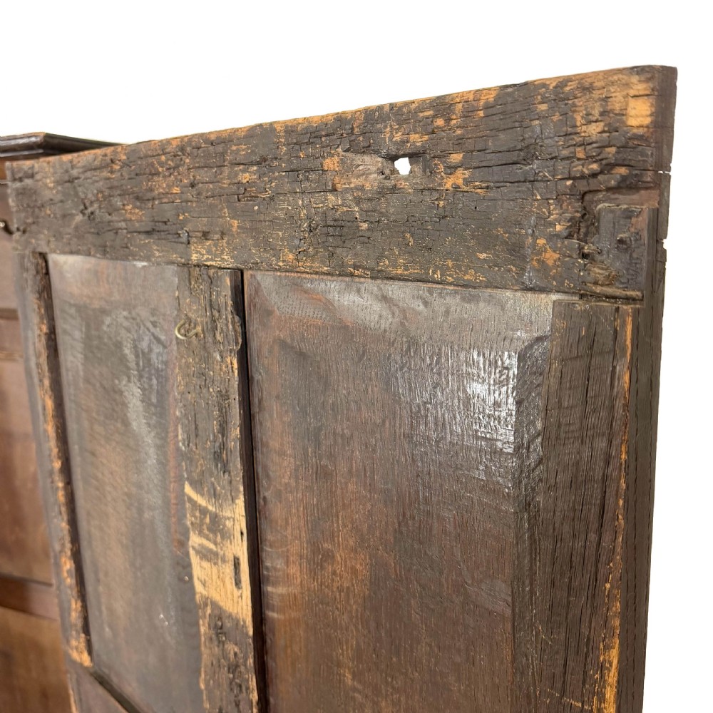 A two-tier dark oak cupboard featuring relief carvings, lion masks, geometric panelled doors, and a decorative carved pediment. View XV
