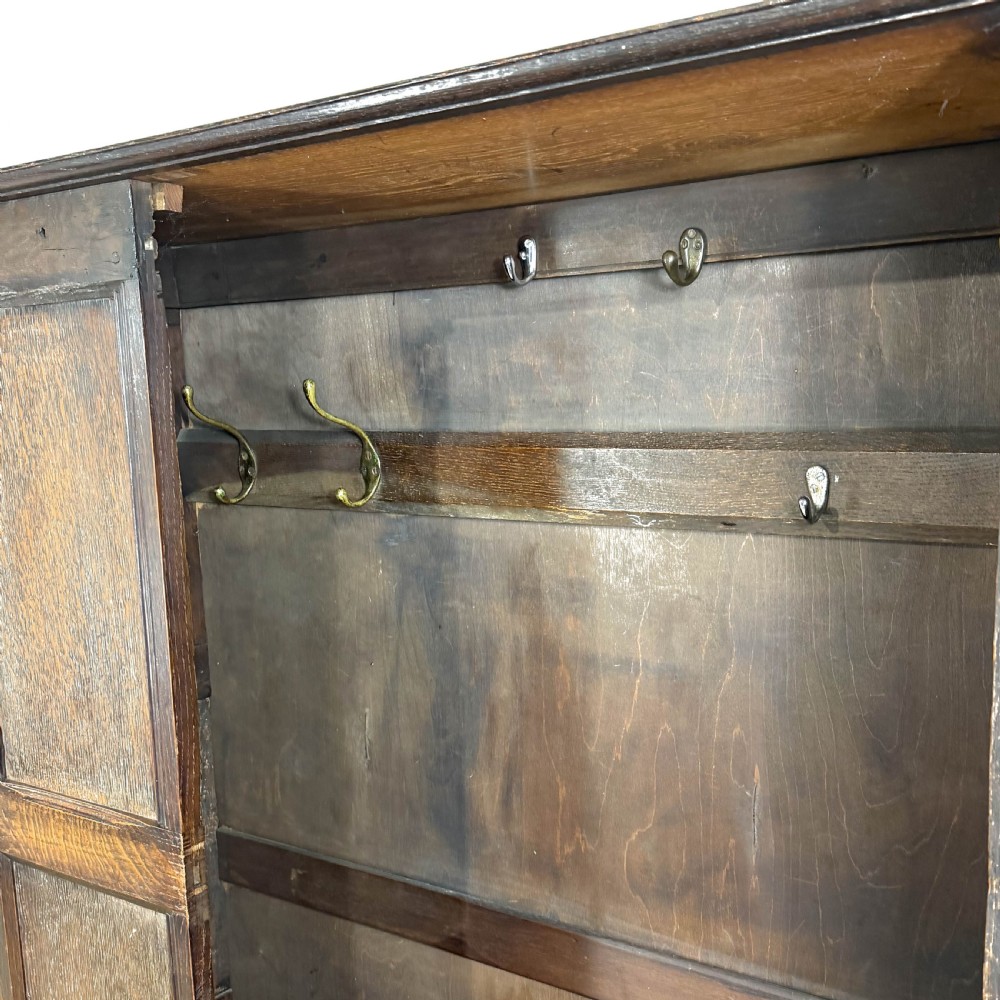 A two-tier dark oak cupboard featuring relief carvings, lion masks, geometric panelled doors, and a decorative carved pediment. View XVI