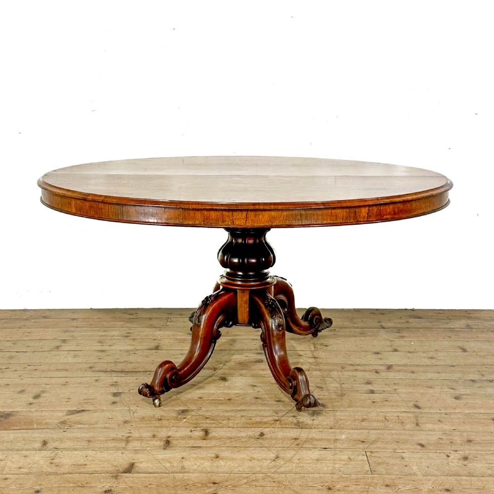 A circular nineteenth-century rosewood loo table supported by a turned central pedestal and four carved scroll legs on castors. View IV