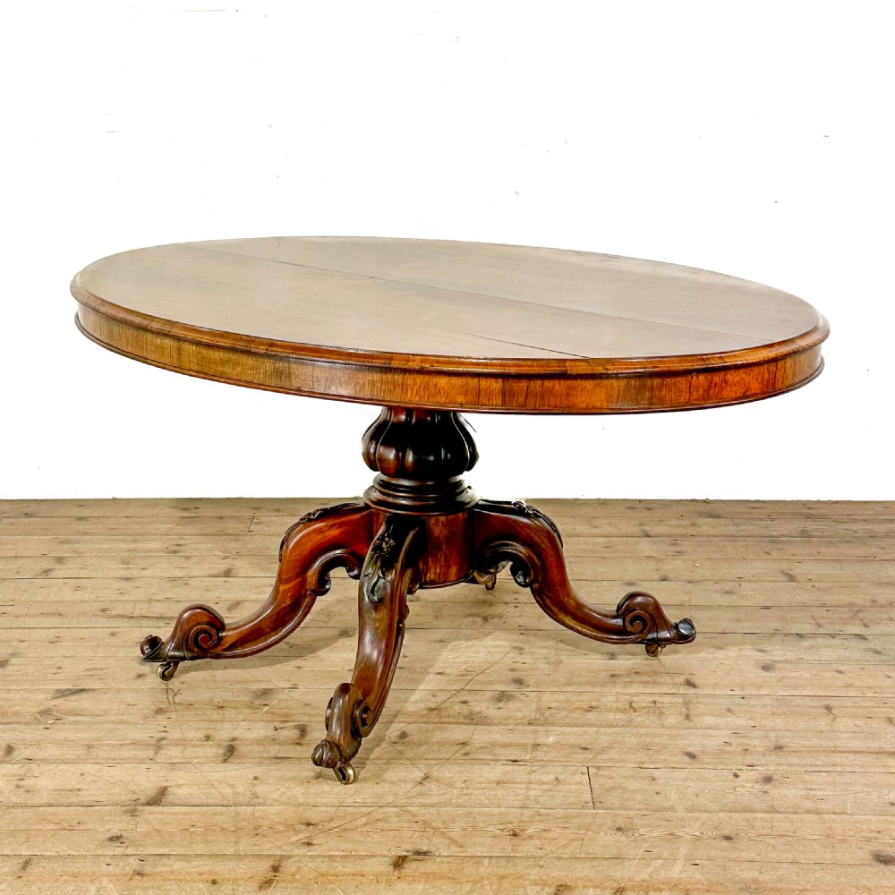 A circular nineteenth-century rosewood loo table supported by a turned central pedestal and four carved scroll legs on castors. View VI