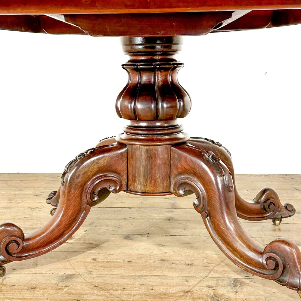 A circular nineteenth-century rosewood loo table supported by a turned central pedestal and four carved scroll legs on castors. View IX