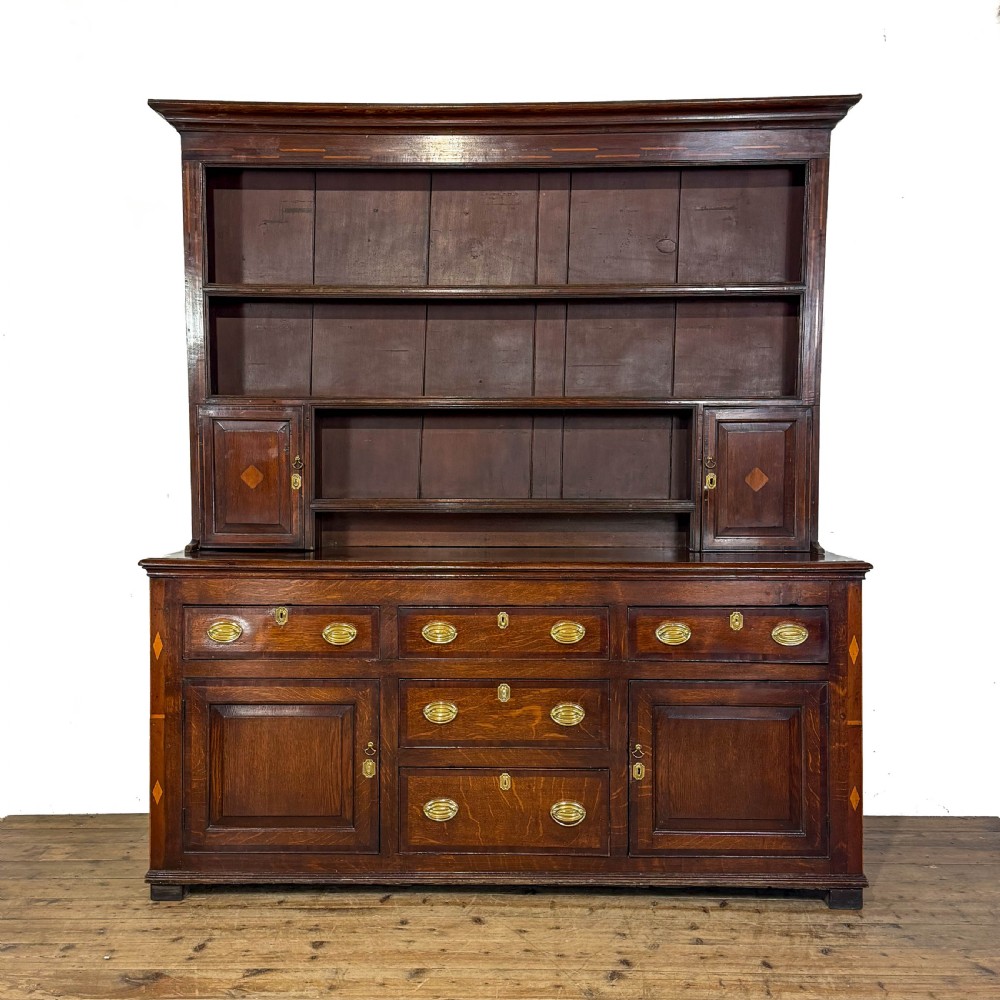 An antique Georgian dark oak dresser featuring an upper shelving rack, small cupboard doors with diamond inlay, and a base containing multiple drawers and panelled cupboards with brass handles.