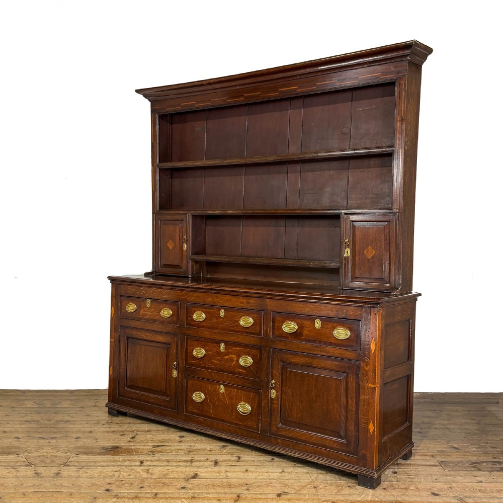 An antique Georgian dark oak dresser featuring an upper shelving rack, small cupboard doors with diamond inlay, and a base containing multiple drawers and panelled cupboards with brass handles. View IV
