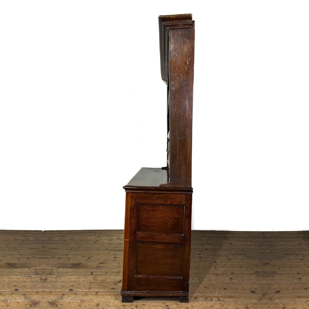 An antique Georgian dark oak dresser featuring an upper shelving rack, small cupboard doors with diamond inlay, and a base containing multiple drawers and panelled cupboards with brass handles. View VI