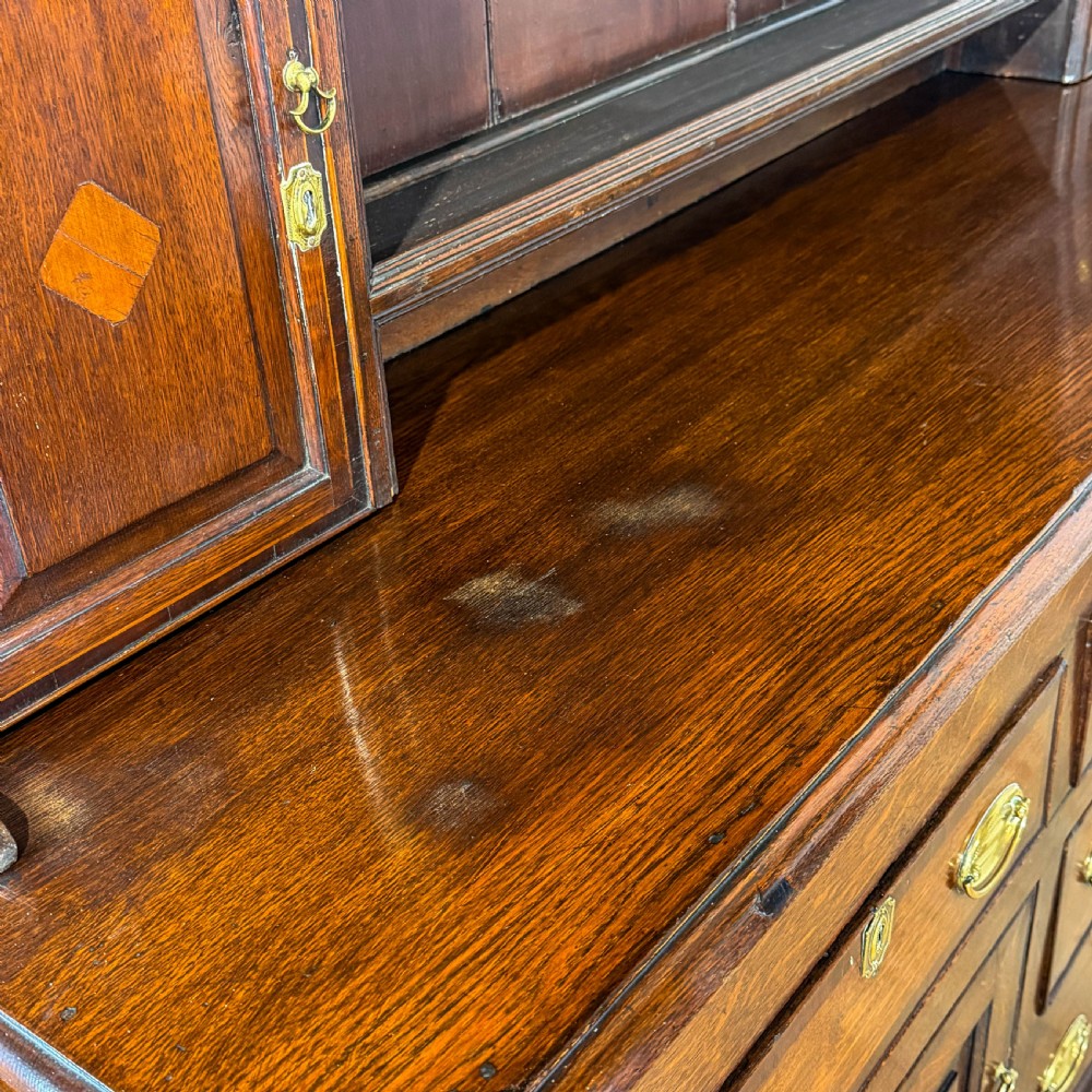 An antique Georgian dark oak dresser featuring an upper shelving rack, small cupboard doors with diamond inlay, and a base containing multiple drawers and panelled cupboards with brass handles. View X