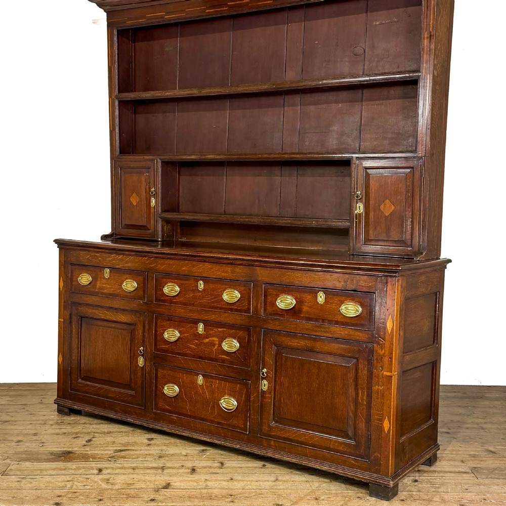 An antique Georgian dark oak dresser featuring an upper shelving rack, small cupboard doors with diamond inlay, and a base containing multiple drawers and panelled cupboards with brass handles. View XI