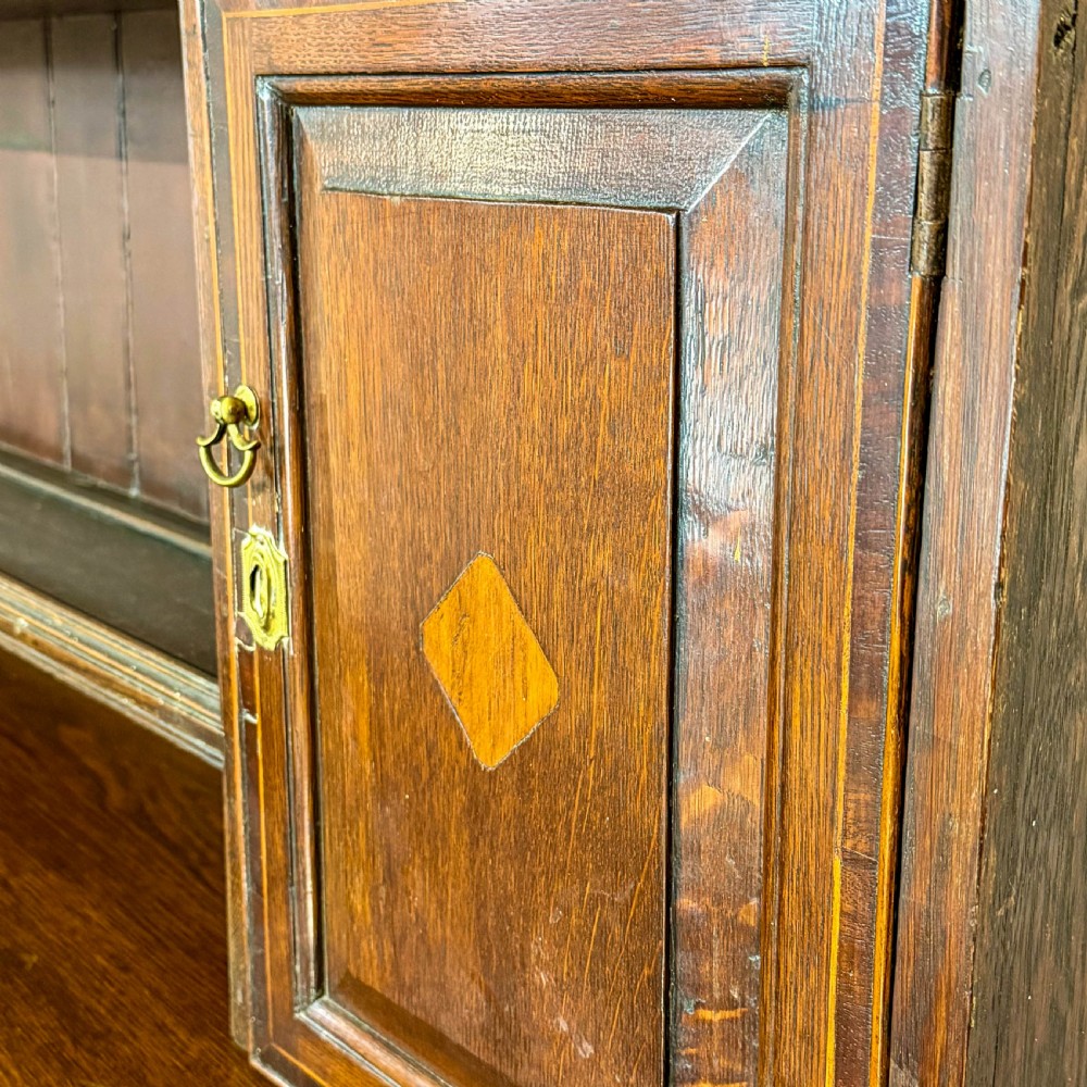 An antique Georgian dark oak dresser featuring an upper shelving rack, small cupboard doors with diamond inlay, and a base containing multiple drawers and panelled cupboards with brass handles. View XII