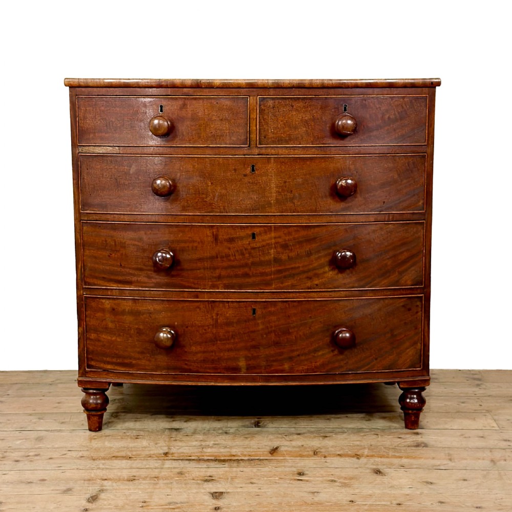 An antique mahogany bow front chest of drawers with two short drawers over three long graduated drawers, turned wooden handles, and turned feet.