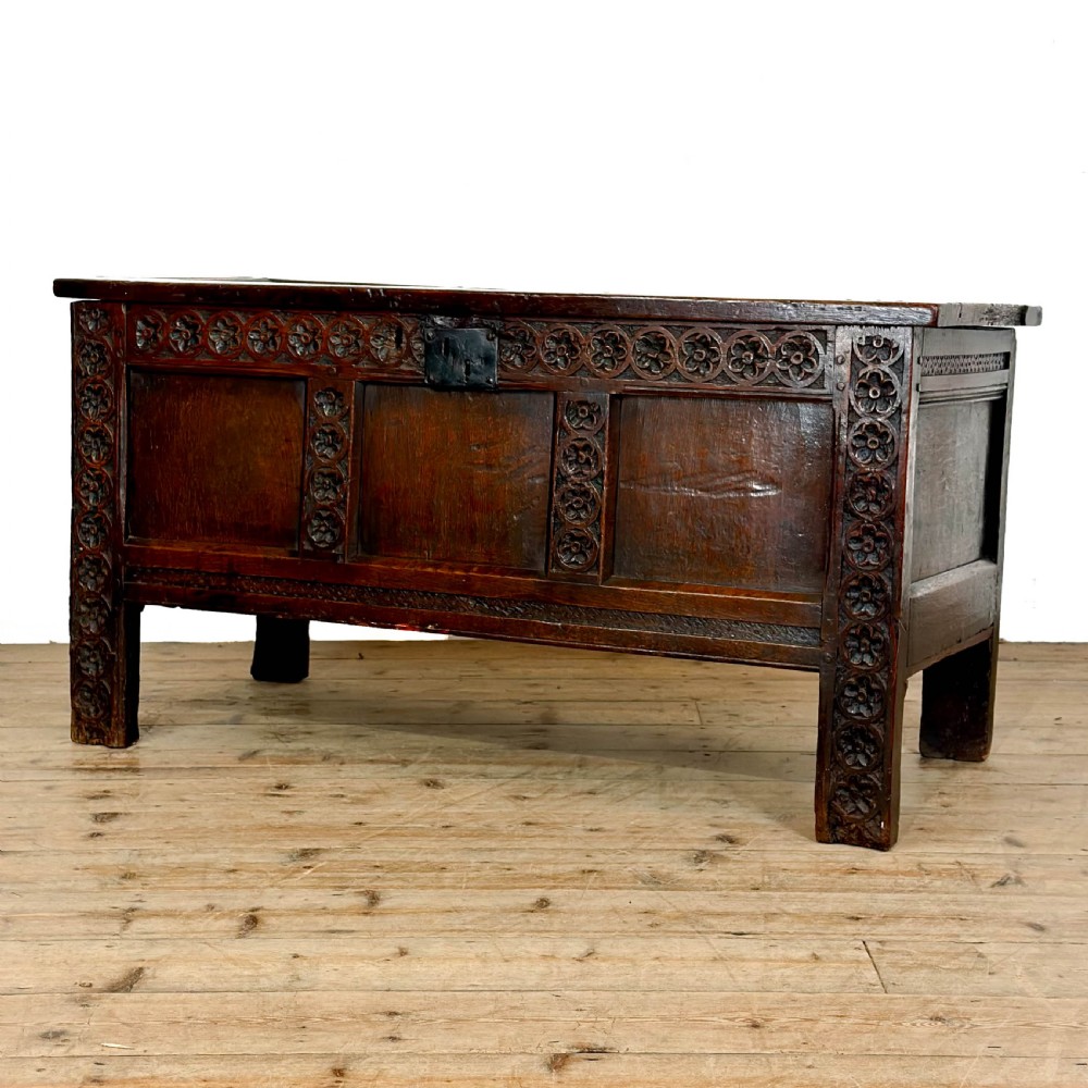 An 18th-century dark oak coffer featuring three carved front panels, a carved floral frieze, a hinged top lid, and an iron lock plate.