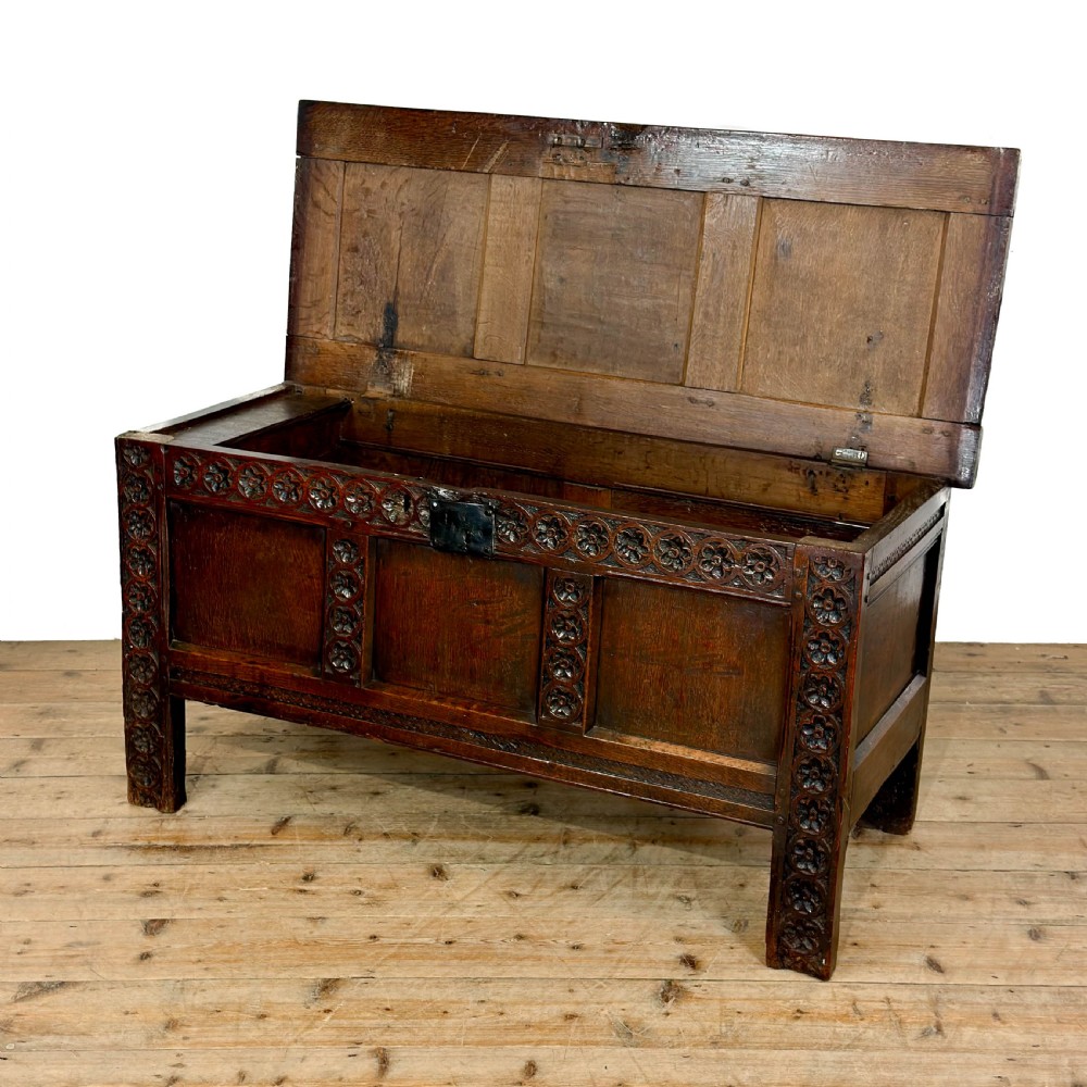 An 18th-century dark oak coffer featuring three carved front panels, a carved floral frieze, a hinged top lid, and an iron lock plate. View II