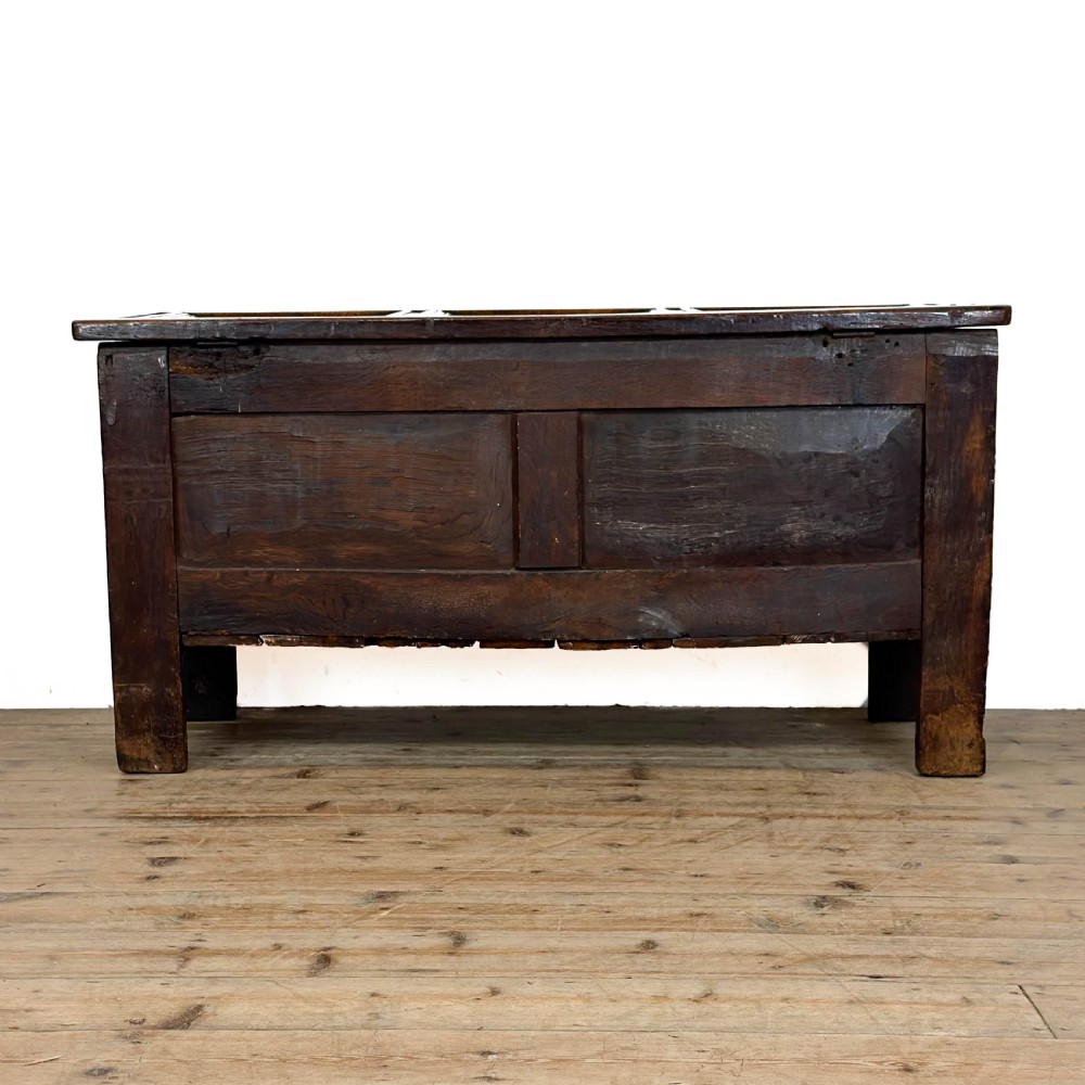 An 18th-century dark oak coffer featuring three carved front panels, a carved floral frieze, a hinged top lid, and an iron lock plate. View V