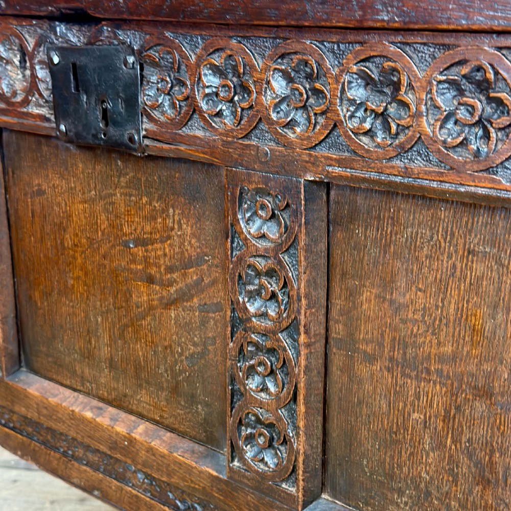 An 18th-century dark oak coffer featuring three carved front panels, a carved floral frieze, a hinged top lid, and an iron lock plate. View VI