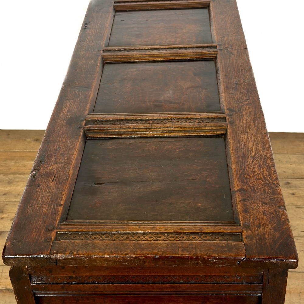 An 18th-century dark oak coffer featuring three carved front panels, a carved floral frieze, a hinged top lid, and an iron lock plate. View XI