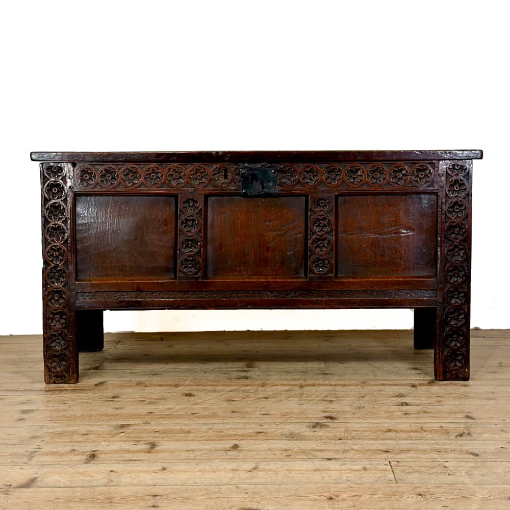 An 18th-century dark oak coffer featuring three carved front panels, a carved floral frieze, a hinged top lid, and an iron lock plate. View XII