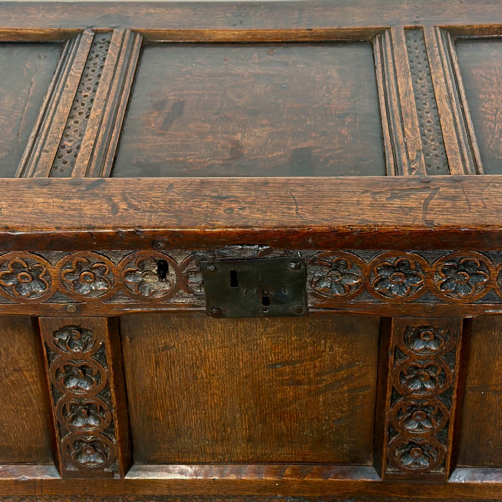 An 18th-century dark oak coffer featuring three carved front panels, a carved floral frieze, a hinged top lid, and an iron lock plate. View XIII