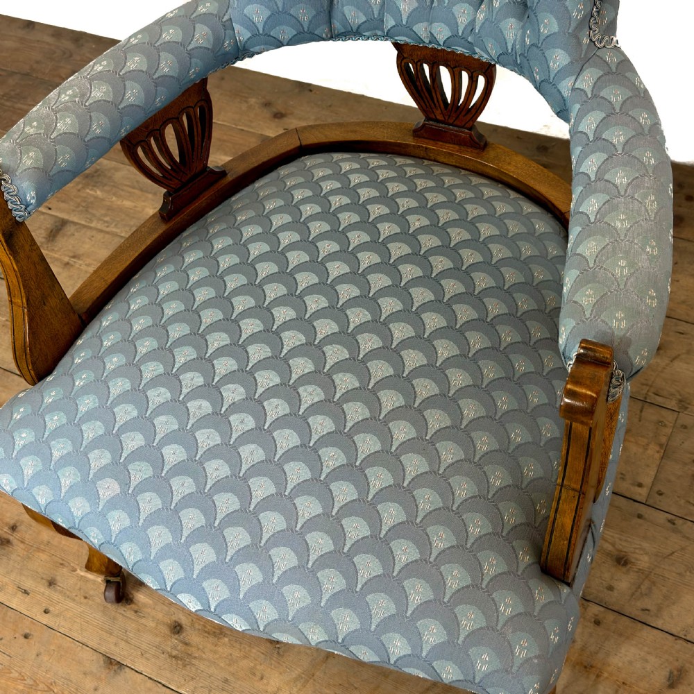 An Edwardian mahogany tub armchair with light blue pattern fabric upholstery, deep-buttoned backrest, and legs on castors. View VI