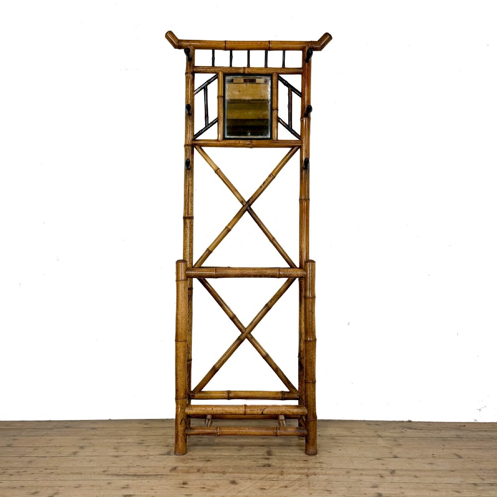 A tall Victorian bamboo hall stand featuring a central rectangular mirror, multiple turned coat pegs, cross-braced framing, and an integrated stick stand base.