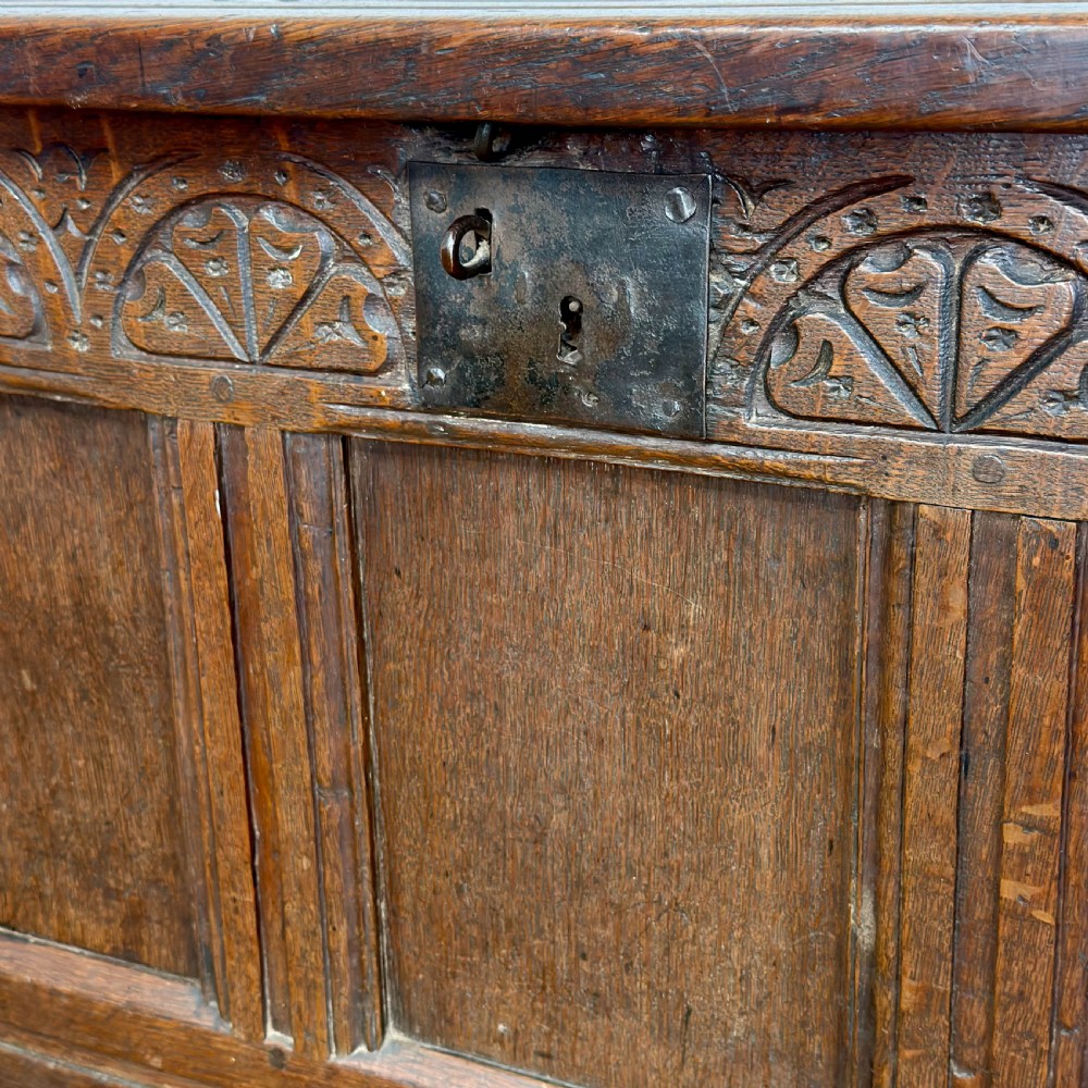 A dark oak coffer with three carved lunette frieze panels above recessed lower panels and an iron lock plate. View X