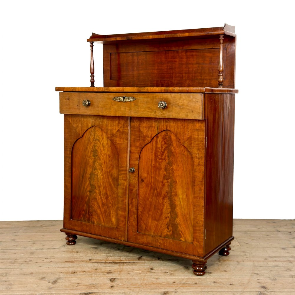 A Victorian mahogany chiffonier sideboard featuring a raised back shelf on turned supports, a frieze drawer with brass hardware, and two arched cupboard doors.