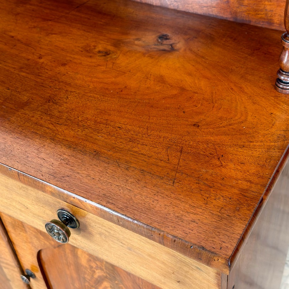 A Victorian mahogany chiffonier sideboard featuring a raised back shelf on turned supports, a frieze drawer with brass hardware, and two arched cupboard doors. View VI