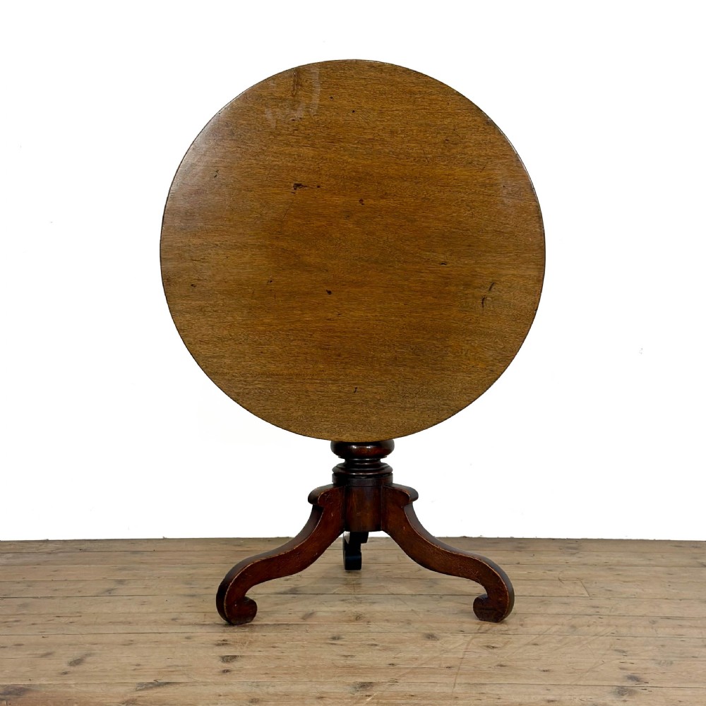 An antique Georgian mahogany tilt top table shown upright with a circular top, turned central pedestal, and tripod legs.