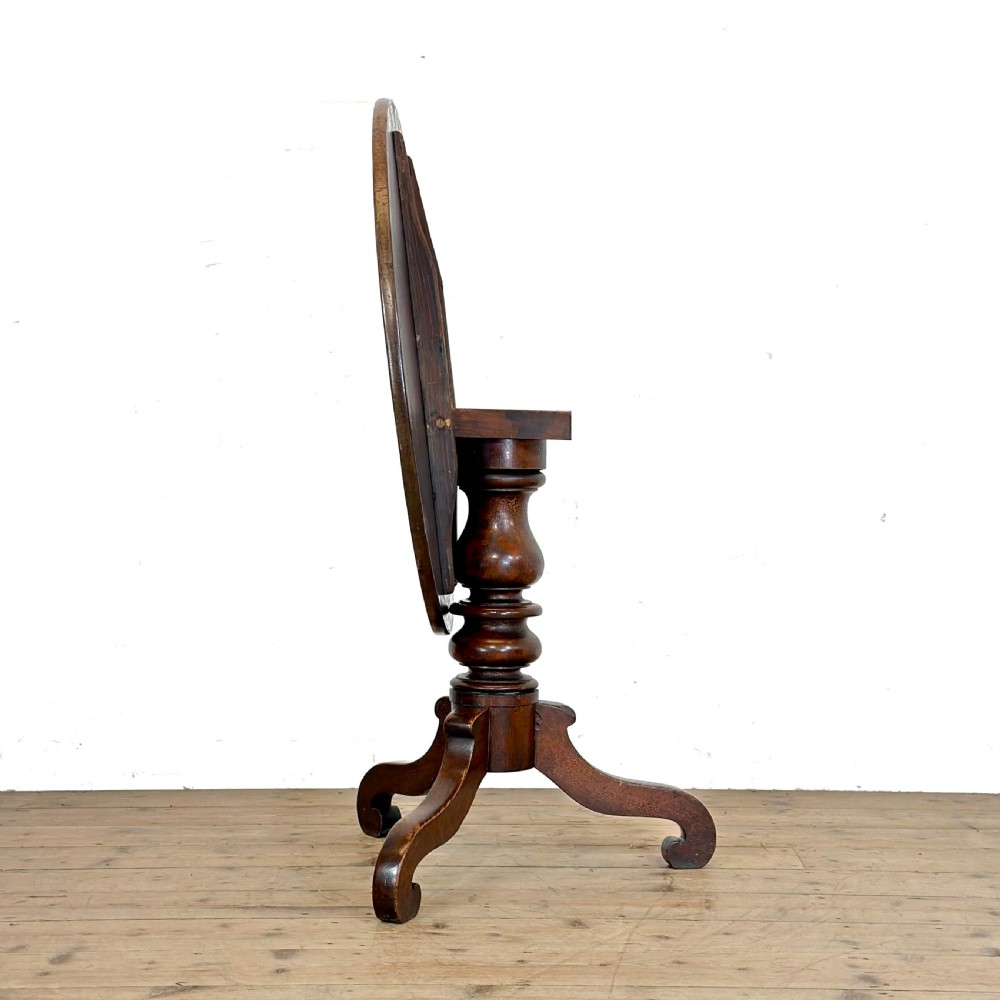 An antique Georgian mahogany tilt top table shown upright with a circular top, turned central pedestal, and tripod legs. View III