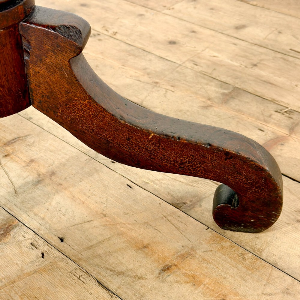 An antique Georgian mahogany tilt top table shown upright with a circular top, turned central pedestal, and tripod legs. View X