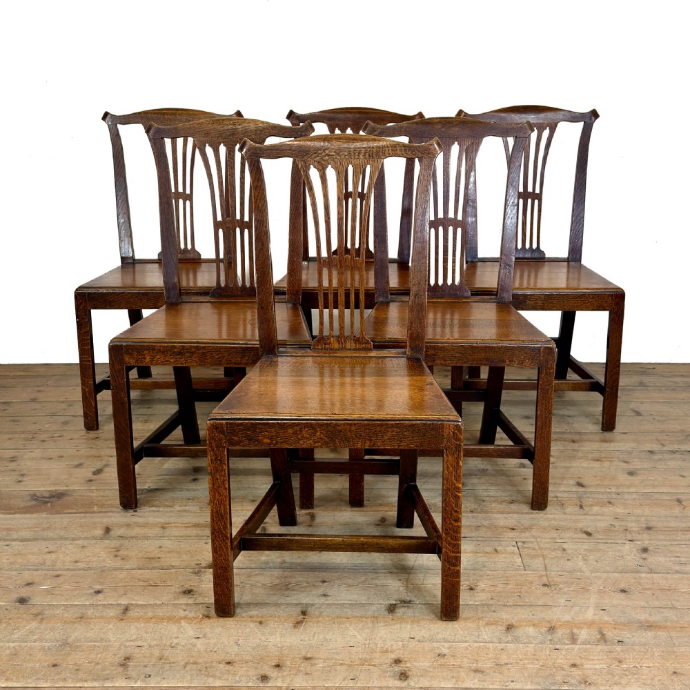 A set of six medium brown antique oak dining chairs featuring vertical splat backs, solid wooden seats, and stretcher bases.