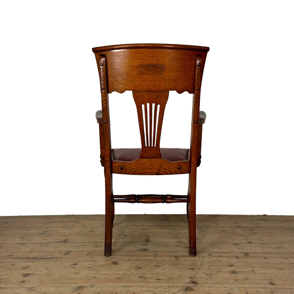 An antique dark oak carver chair featuring a carved splat backrest, curved armrests, turned stretchers, and a padded red leather seat with brass studs. View IV