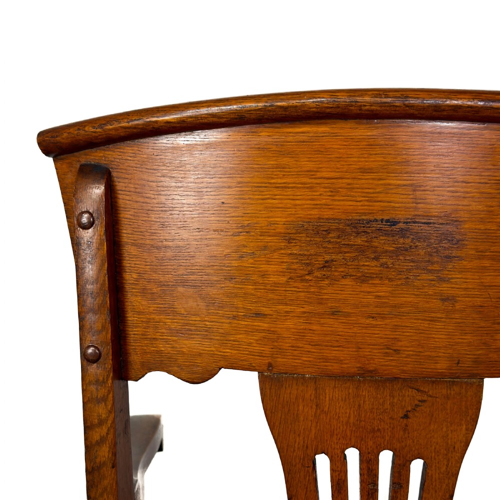 An antique dark oak carver chair featuring a carved splat backrest, curved armrests, turned stretchers, and a padded red leather seat with brass studs. View VIII