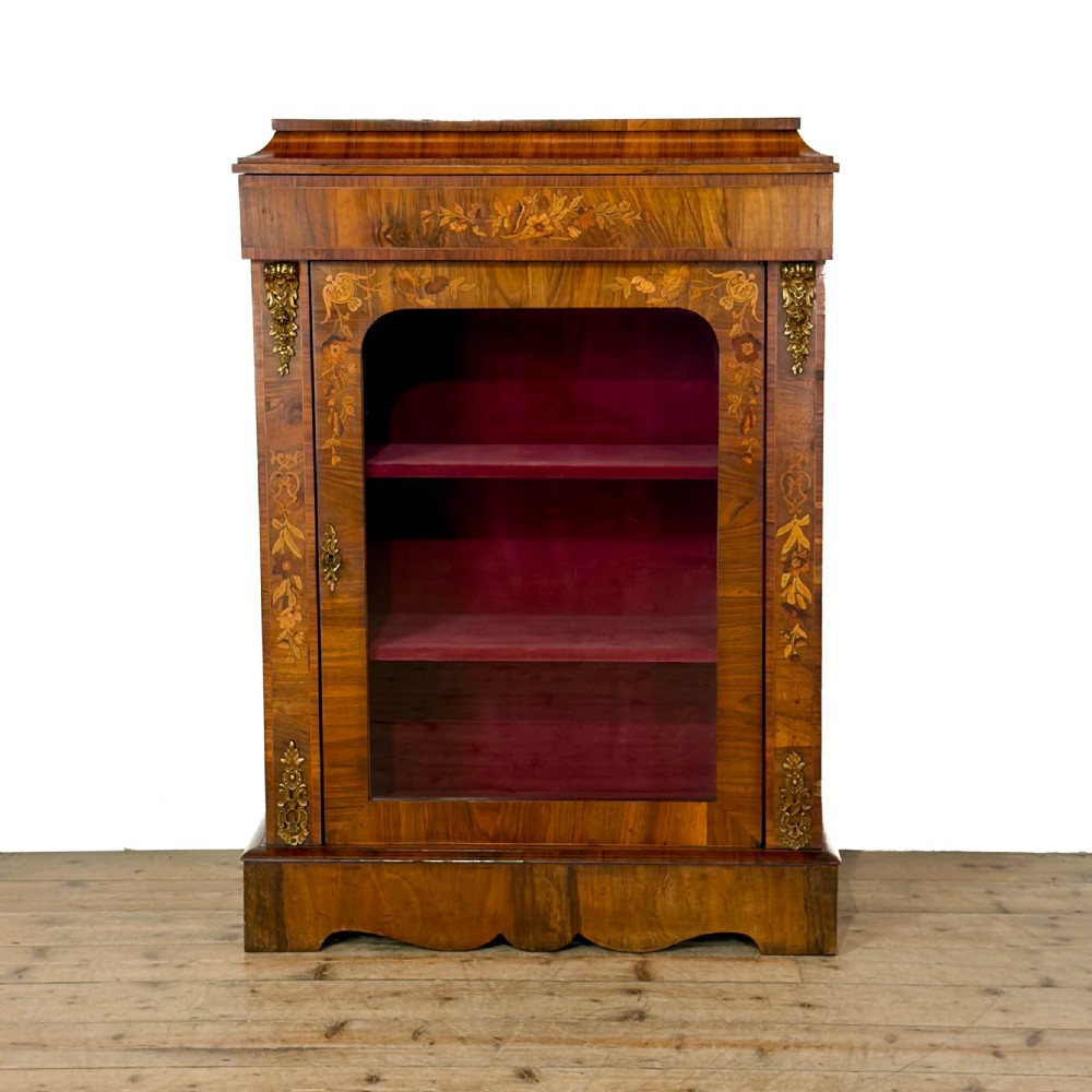 A Victorian walnut pier cabinet featuring floral marquetry inlays, gilt metal mounts, a single glazed door, and a red fabric-lined interior with two shelves.