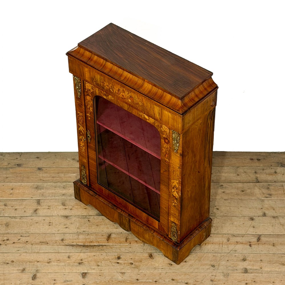 A Victorian walnut pier cabinet featuring floral marquetry inlays, gilt metal mounts, a single glazed door, and a red fabric-lined interior with two shelves. View V
