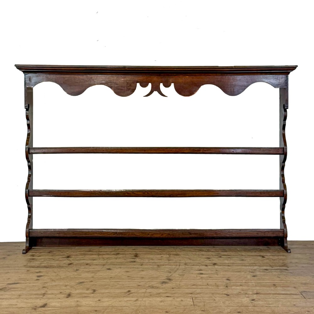 A dark oak wooden dresser rack featuring three horizontal shelves and a scalloped top frieze.