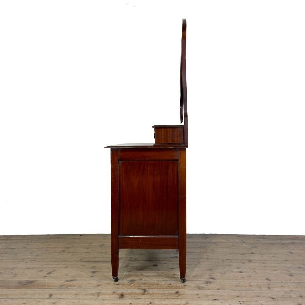 An Edwardian mahogany dressing table featuring an oval swivel mirror, satinwood stringing inlay, multiple drawers with brass handles, and square tapered legs on castors. View II