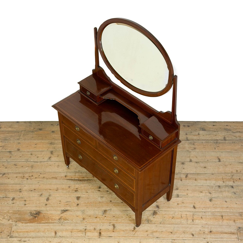 An Edwardian mahogany dressing table featuring an oval swivel mirror, satinwood stringing inlay, multiple drawers with brass handles, and square tapered legs on castors. View III