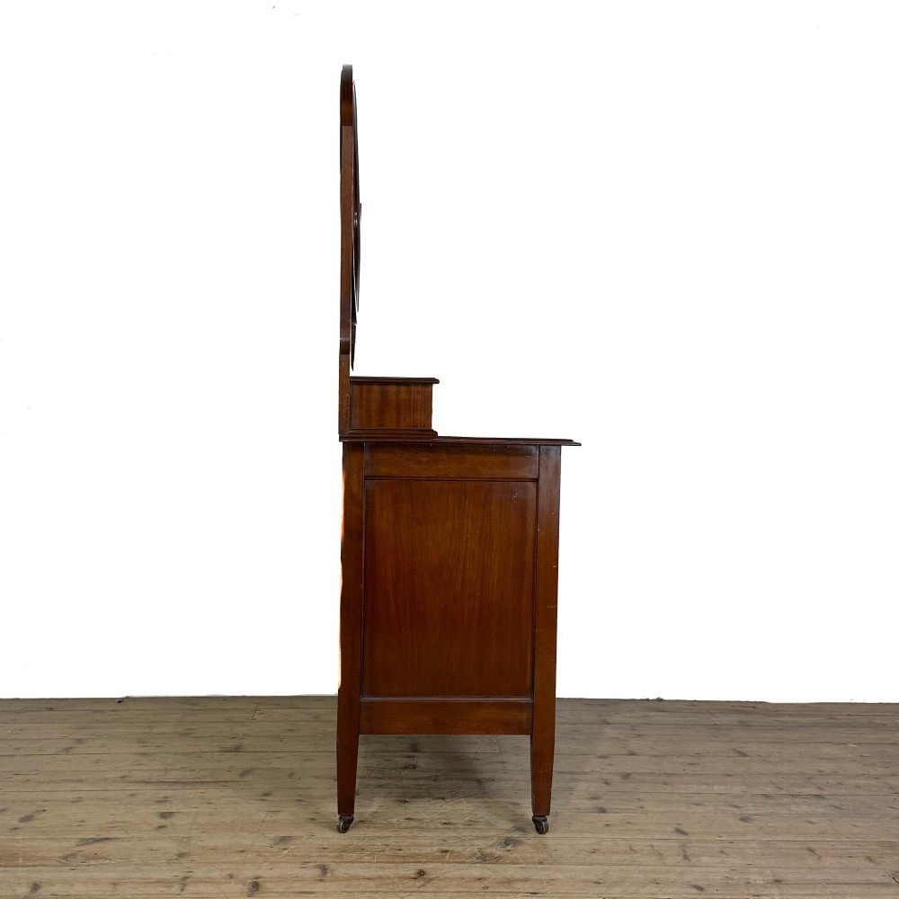 An Edwardian mahogany dressing table featuring an oval swivel mirror, satinwood stringing inlay, multiple drawers with brass handles, and square tapered legs on castors. View IV