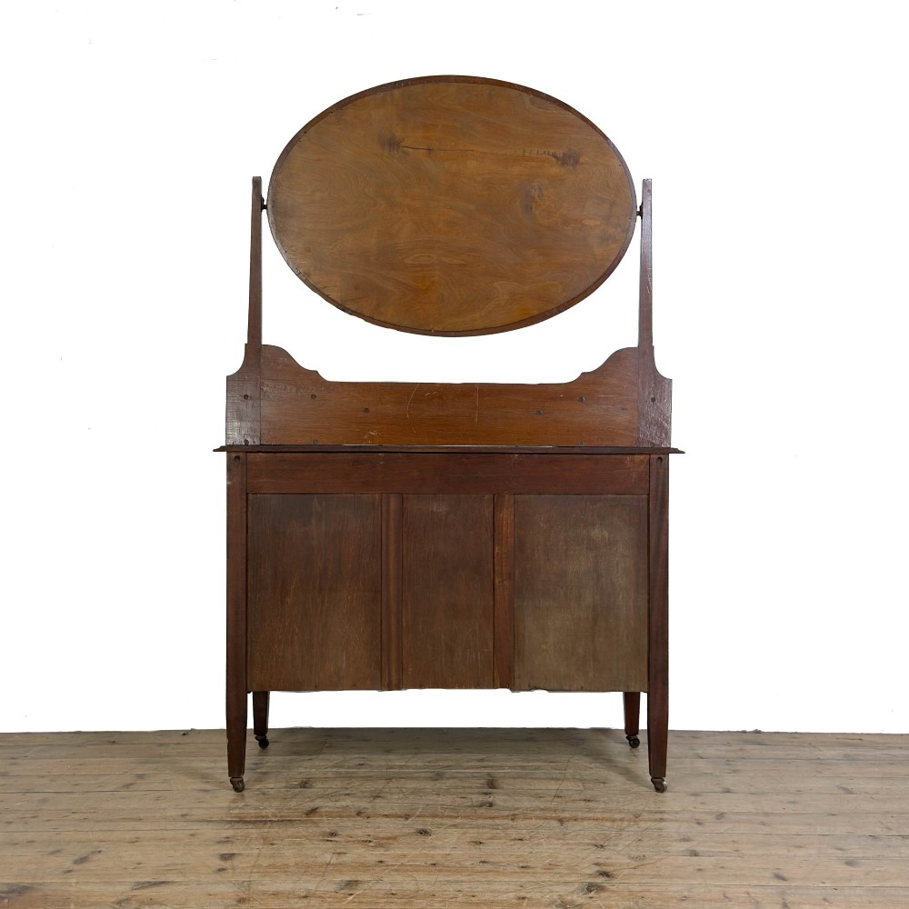 An Edwardian mahogany dressing table featuring an oval swivel mirror, satinwood stringing inlay, multiple drawers with brass handles, and square tapered legs on castors. View V
