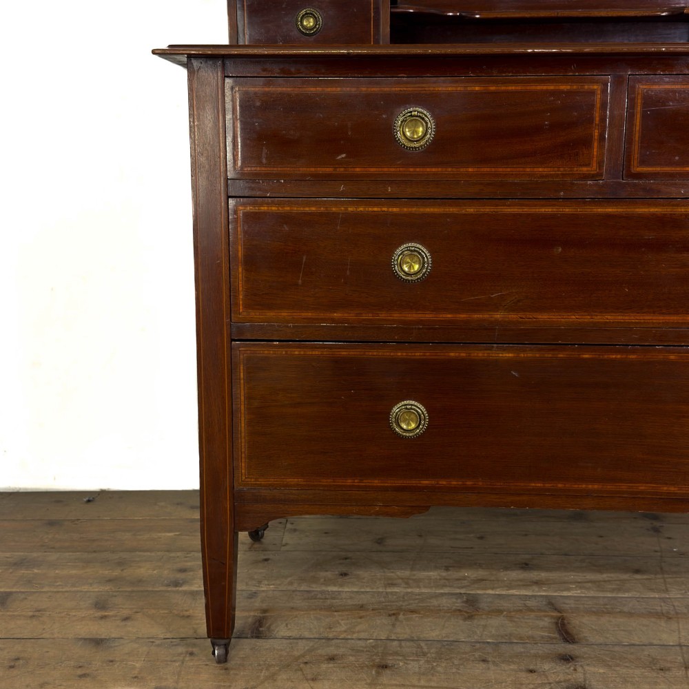 An Edwardian mahogany dressing table featuring an oval swivel mirror, satinwood stringing inlay, multiple drawers with brass handles, and square tapered legs on castors. View VII