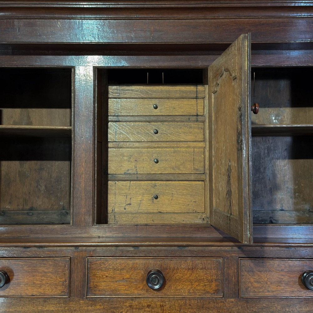 An 18th-century dark oak Welsh cwpwrdd deuddarn cupboard featuring two tiers with arched panelled doors and three lower drawers. View X