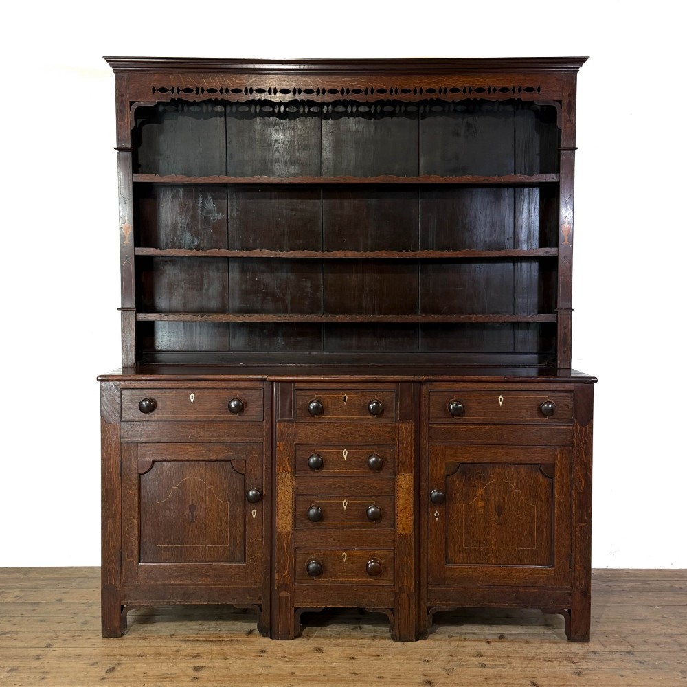 An antique 19th-century dark oak North Wales dresser featuring an open three-shelf plate rack with a pierced fretwork frieze above a base with two cupboards and four central drawers.