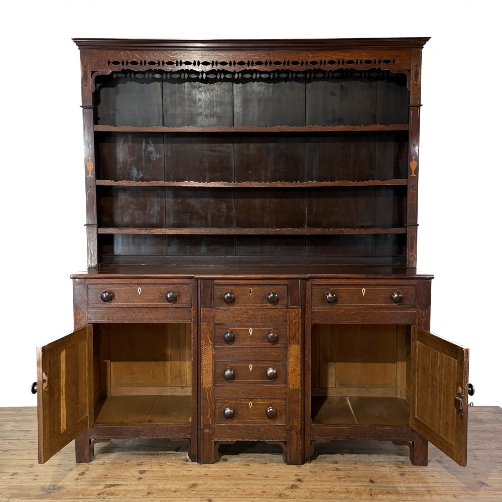 An antique 19th-century dark oak North Wales dresser featuring an open three-shelf plate rack with a pierced fretwork frieze above a base with two cupboards and four central drawers. View II